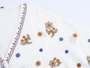 Detail of colorful floral embroidery on a white V-neck long sleeve cotton blouse