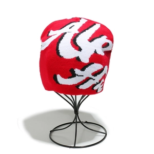 Detailed close-up of red knit beanie featuring white jacquard letter patterns and thick texture