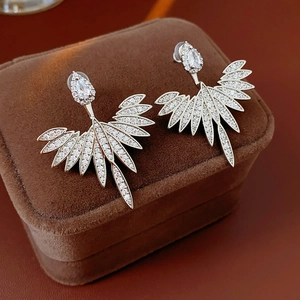 Detailed macro view of silver wing earrings with white zircon on a brown velvet box