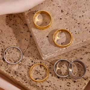 Flat lay of six minimalist 18K gold and silver plated stainless steel band rings on stone