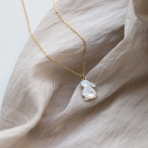 Détail d'un pendentif lapin en nacre blanche sur chaîne dorée sur fond de tissu en lin