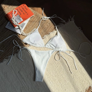 Flat lay of white string bikini with pearl sheen on textured rug with art books
