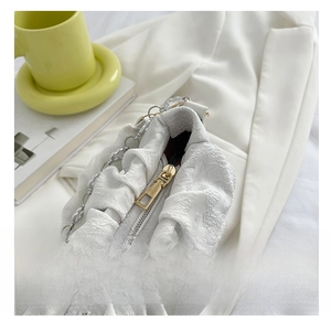 Detail of smooth gold zipper and silver chain on a white pleated texture handbag