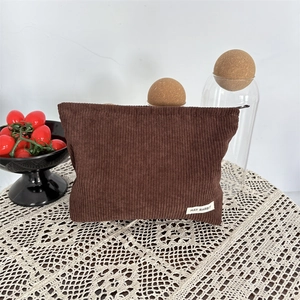 Detail of a brown corduroy cosmetic bag on a white lace tablecloth with lifestyle props