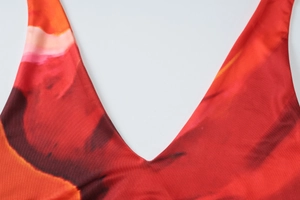 Detail shot of the deep V-neckline featuring a vibrant red-orange abstract floral print
