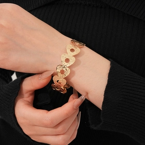 Detail of gold-tone hollow heart cuff with hammered metal texture on woman wrist