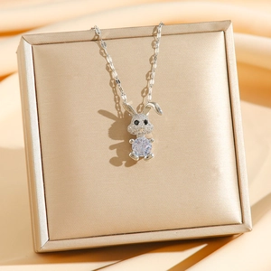 Collana con coniglio e ciondolo in zircone su scatola dorata con sfondo in seta champagne