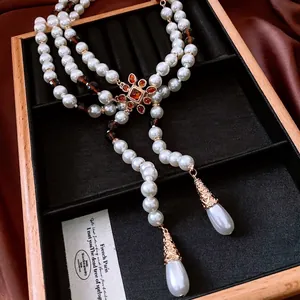 Three-layer faux pearl necklace with a vintage gold floral pendant and teardrop charms