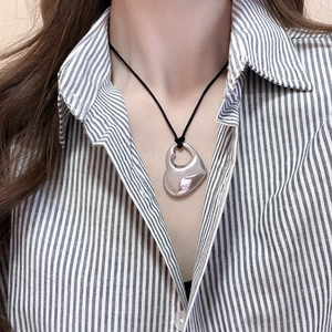 Close-up of hollow double heart silver pendant on black cord worn with striped shirt