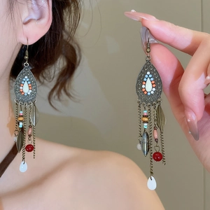Detail of vintage bohemian tassel earrings with beads and metal feather charms on model
