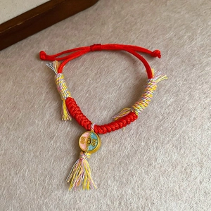 Détail du bracelet tressé rouge avec pendentif émaillé Fú et glands en soie colorés