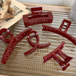 Five assorted burgundy hair claws in various elegant shapes on a textured glass tray