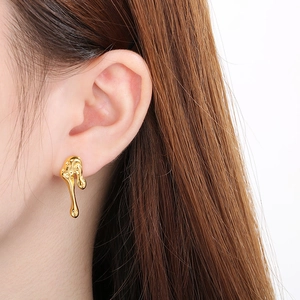 Close-up of golden irregular teardrop earring with liquid metal texture on female model