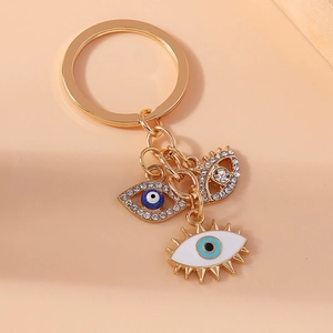 Golden evil eye keychain featuring blue rhinestones and enamel charms on beige background