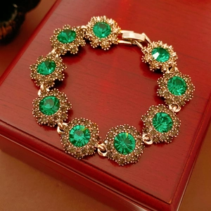 Detailed view of vintage gold flower bracelet with green crystals on a wooden jewelry box