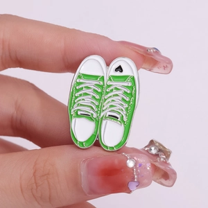 Detail of green canvas shoe enamel pins with heart detail held in hand on purple backdrop