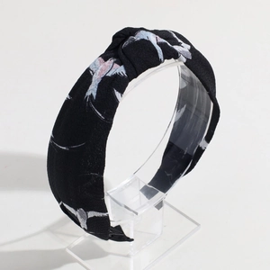 Detail shot of black knitted knotted headband featuring white bird pattern on a stand