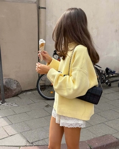 Side view of a woman wearing a loose yellow letter knit sweater with lace shorts in street