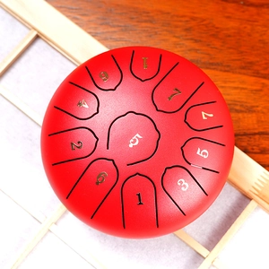 Red 8-note steel tongue drum with golden scale numbers on a minimalist wood background