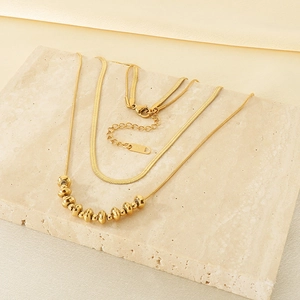 Detail of layered 18K gold-plated snake chain and beaded necklace on a stone base