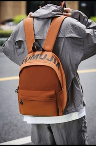Orange nylon backpack for students featuring UMUJIA letter print on a city street background