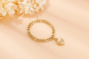 Macro detail of a gold heart pendant on a chunky flat link stainless steel chain bracelet
