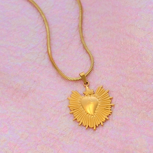 Gros plan du collier avec pendentif cœur sacré doré, détails de couronne et flamme