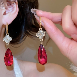Macro detail of gold flower earrings with red teardrop crystals and diamond accents