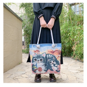 Close-up of woven tote bag with cat and goldfish print and braided cotton rope handles