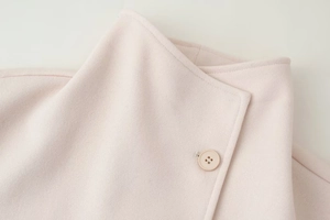 Detail of light pink wool coat lapel and matching button with soft fabric texture