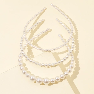 Detailed view of three pearl headbands with various faux pearl sizes on beige background