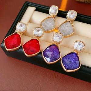 Gros plan de boucles d'oreilles vintage avec pierres rouges, grises et violettes sur boîte