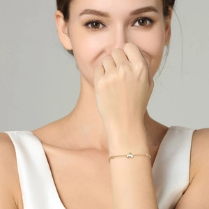 Detail of a gold heart charm bracelet with small stones worn on a female wrist