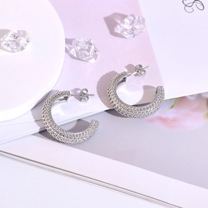 Close-up of silver C-shaped hoop earrings with a textured woven glitter finish