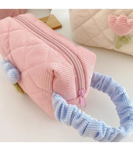 Close-up of pink quilted corduroy makeup bag with blue ruffled handle and floral detail