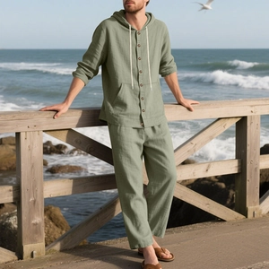 Detail of sage green linen hoody shirt and trousers set worn at a coastal beach setting