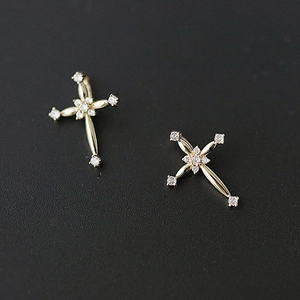 Detailed shot of gold cross stud earrings with sparkling crystals on black surface