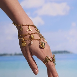 Bracelet océan plaqué or 18K avec breloques coquillages et perles sur fond de plage