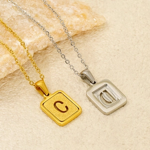Square stainless steel initial pendants with sandblasted texture on a natural stone block