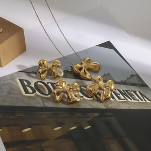Golden bow-shaped necklace and earrings set displayed on a wooden prop and magazine