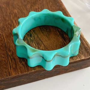 Detailed close-up of a mint green resin wavy bangle with marble texture on wood base