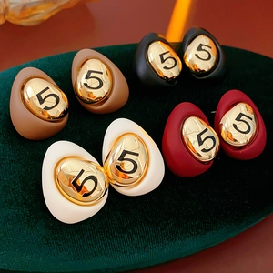 Detail view of retro gold-plated teardrop earrings with number five on green velvet