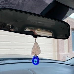 Pink raw crystal and blue evil eye pendant hanging on a car rearview mirror