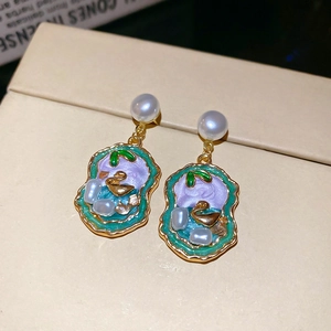 Detail view of pearl earrings with golden swan lake enamel pendants in a jewelry box