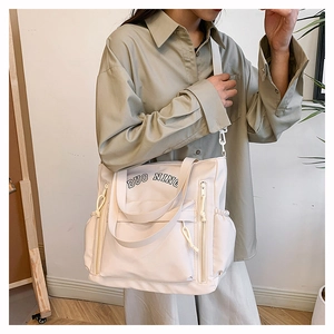 Close-up of a large beige canvas tote bag with multi-pocket design shown on a model