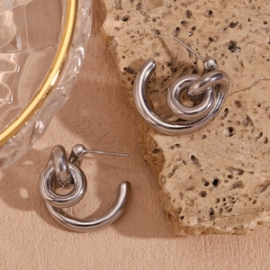 Macro view of interlocking silver C-shaped earrings on textured stone and glass