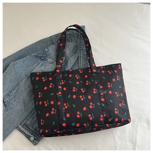 Detailed top view of black cherry print nylon tote bag next to a denim jacket
