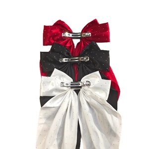 Détail de trois barrettes à nœud en satin rouge noir et blanc ornées de strass