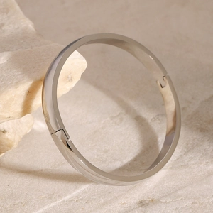 Polished silver stainless steel bangle with clasp closure on minimalist stone background