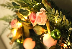 Close-up of Christmas wreath with pink roses, golden baubles, pine cones and warm LED lights